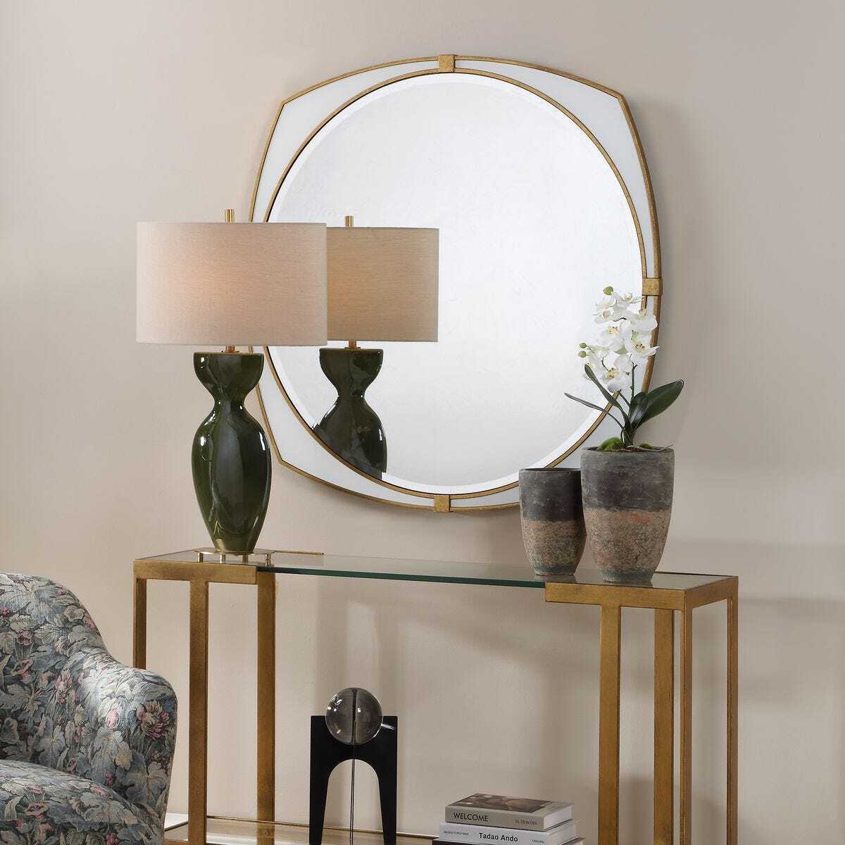 Decorative table with lamp, mirror, and plants against a beige wall.