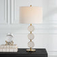 White and gold table lamp with round circle on a console with books and accessory.