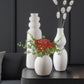 Ceramic white vases with flowers on black end table with black walls.