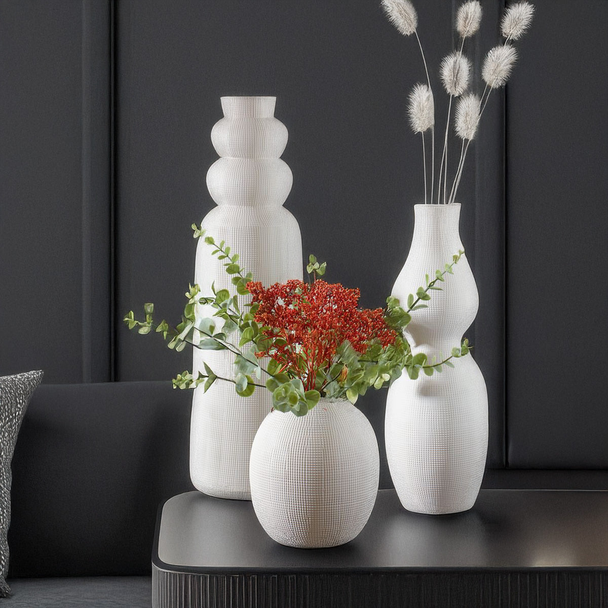 Ceramic white vases with flowers on black end table with black walls.