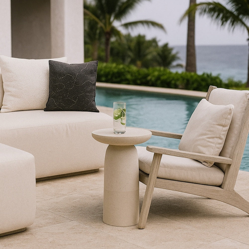Outdoor patio setting with beige furniture and a glass of water by a poolside.