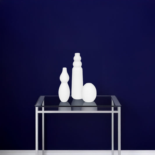 Set of 3 White Modern Geometric Vases on a Glass Console Table against a navy wall.