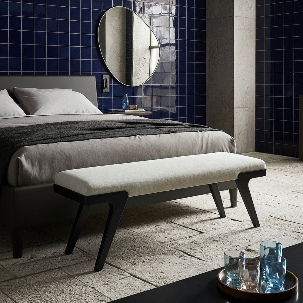 Modern bedroom with a bed, bench, and decorative items against a blue tiled wall.