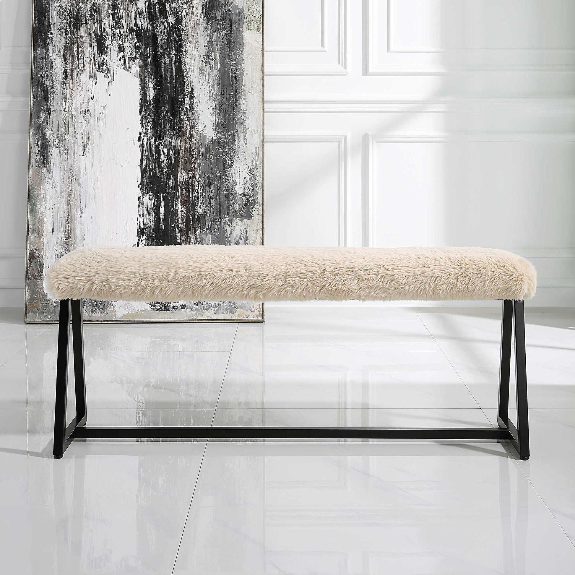 Bench made with white sherpa cushion and black metal frame with large abstract art in the background.