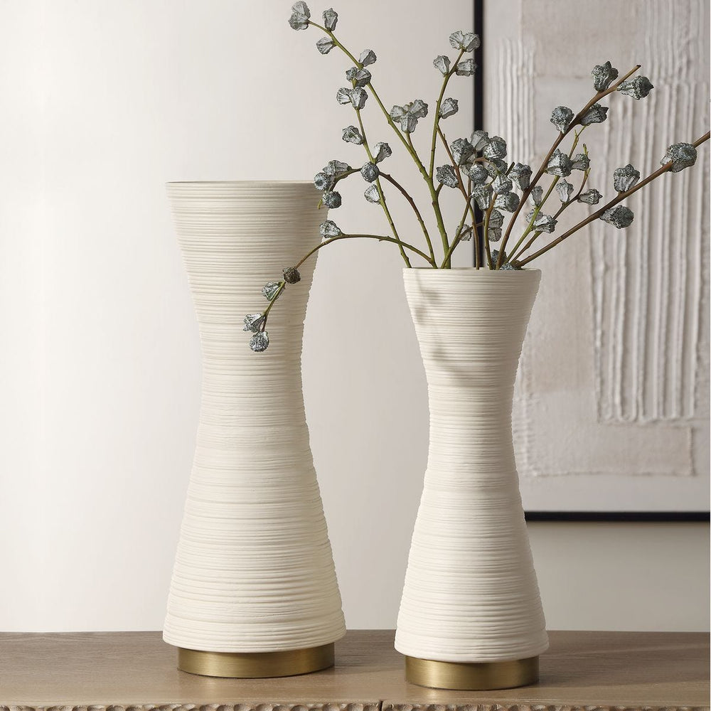 Two white textured vases with gold bases on a light wooden surface.
