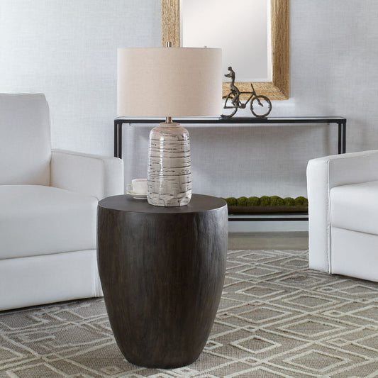 Wood drum side table with white table lamp and geometric rug and white decorative chairs in a transitional living room.