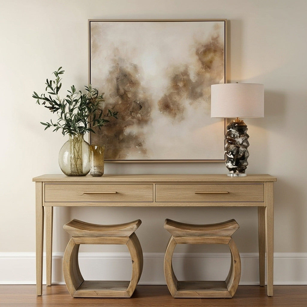 Wooden console table with two stools, a lamp, and decorative items against a wall with abstract art.