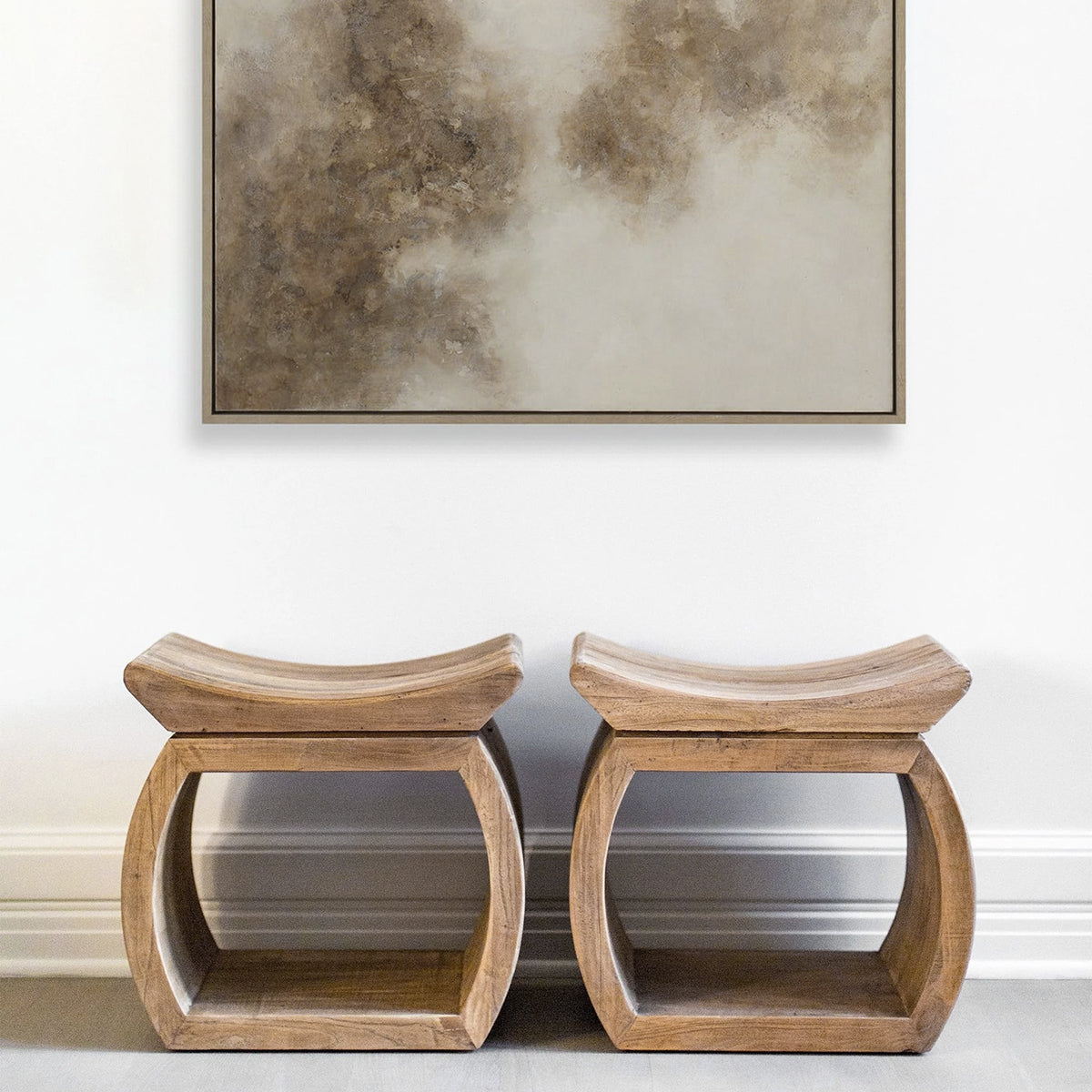 Two wooden stools against a white wall with a textured painting above them.