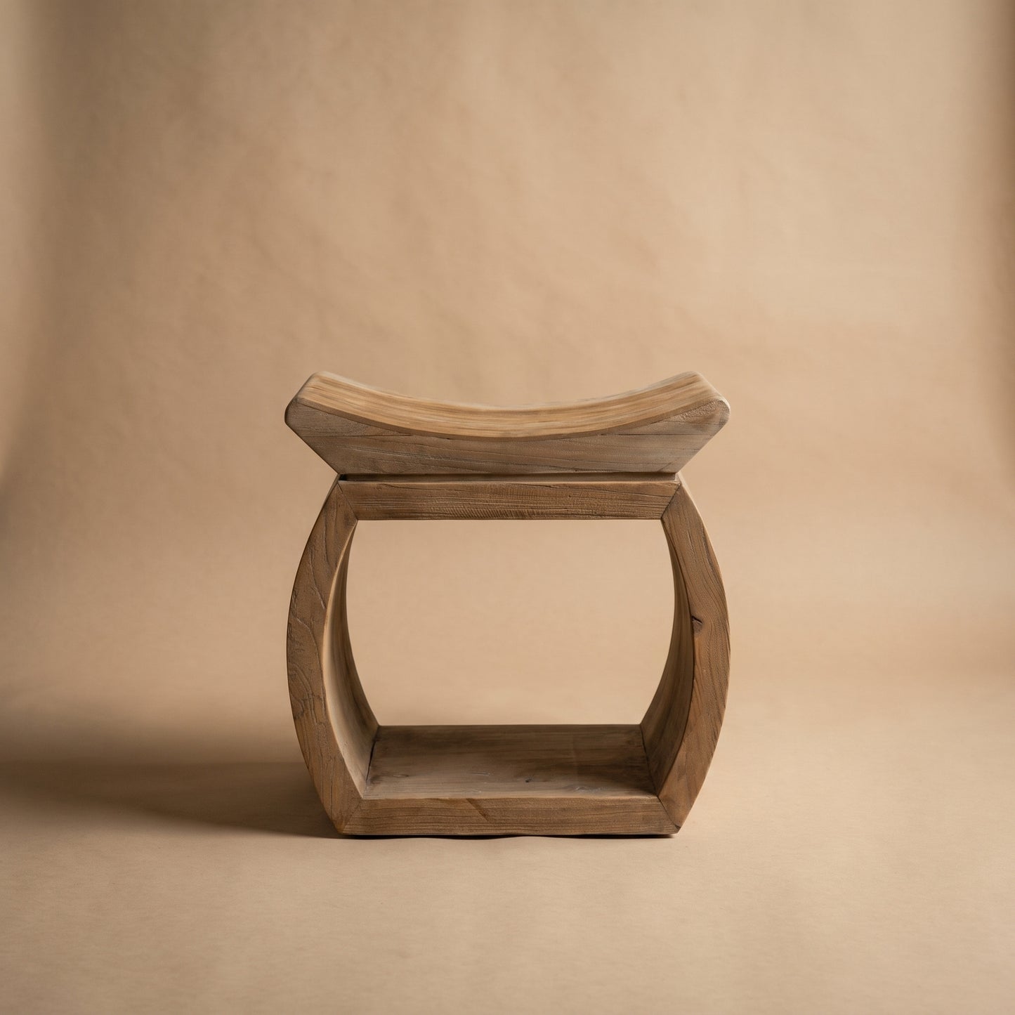 A rustic wooden stool with a curved seat and a square frame base, photographed against a neutral beige background.