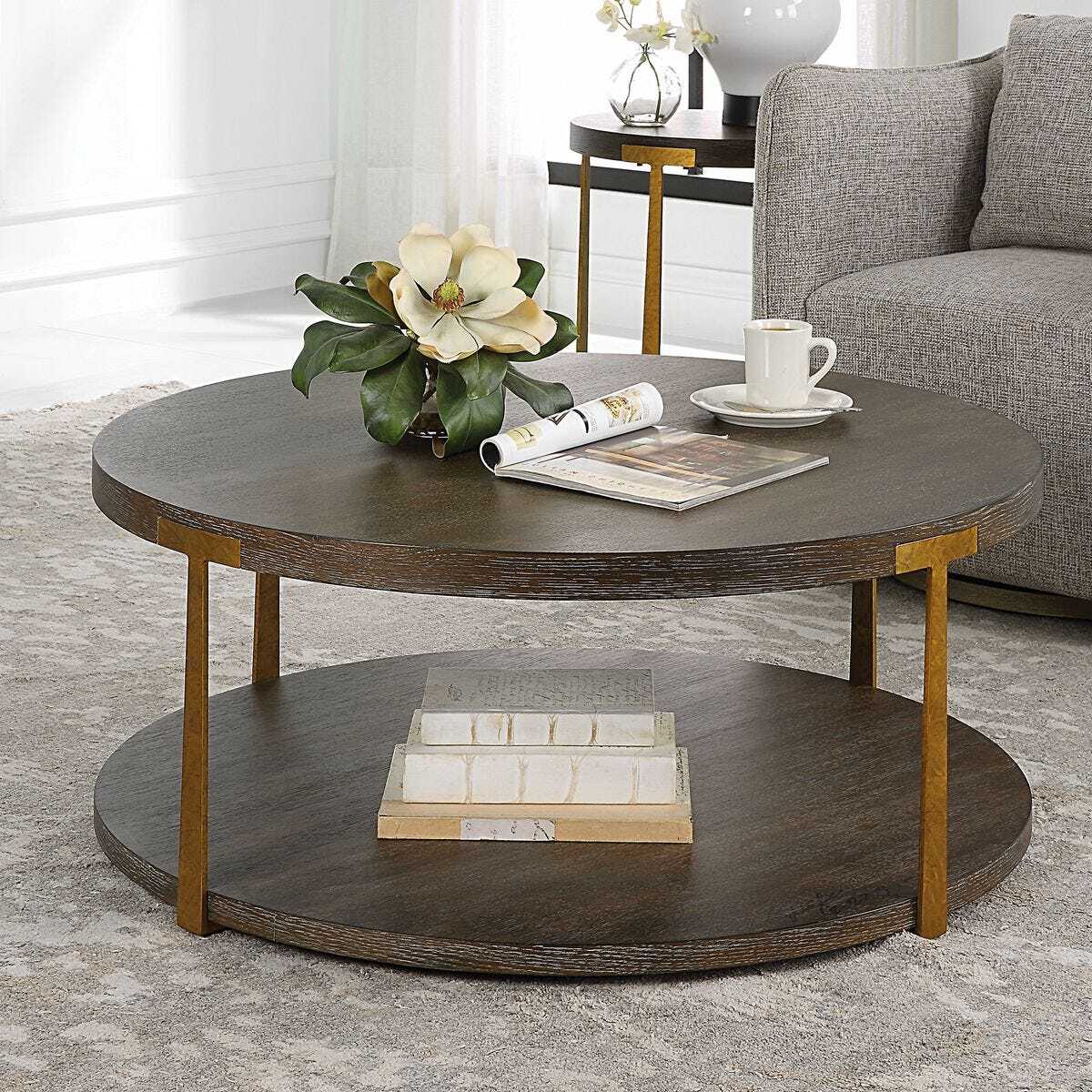 Round wooden coffee table with a magazine, cup, and decorative items in a living room setting.