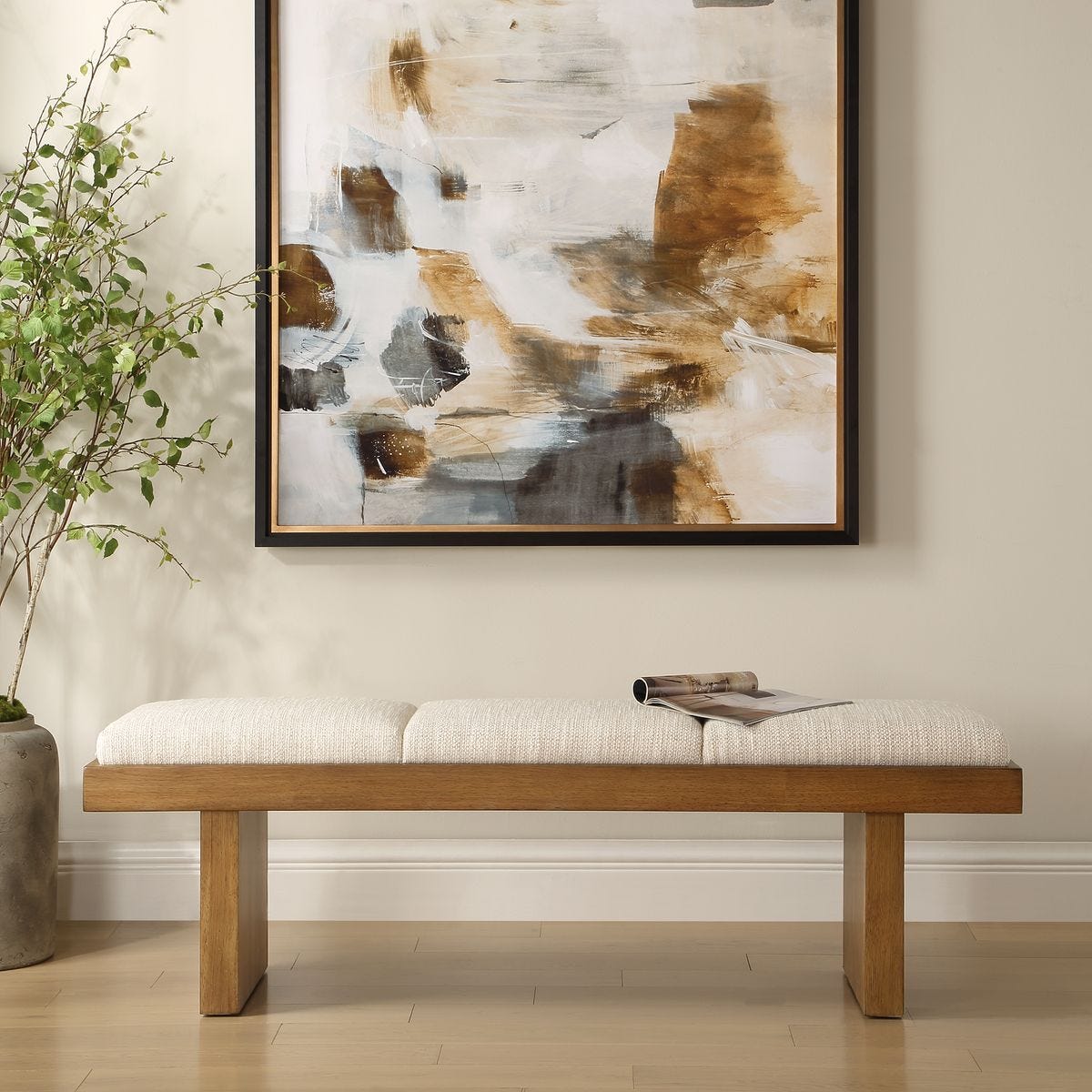 Wooden bench with white cushion in front of a abstract painting on a beige wall.
