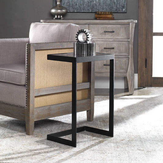 Acantilever designed table with classic style, features thick aged black iron with an open framed base, and a mirrored top with linear antiquing and distressed edges. THis table is nestled up to an occasional chair.