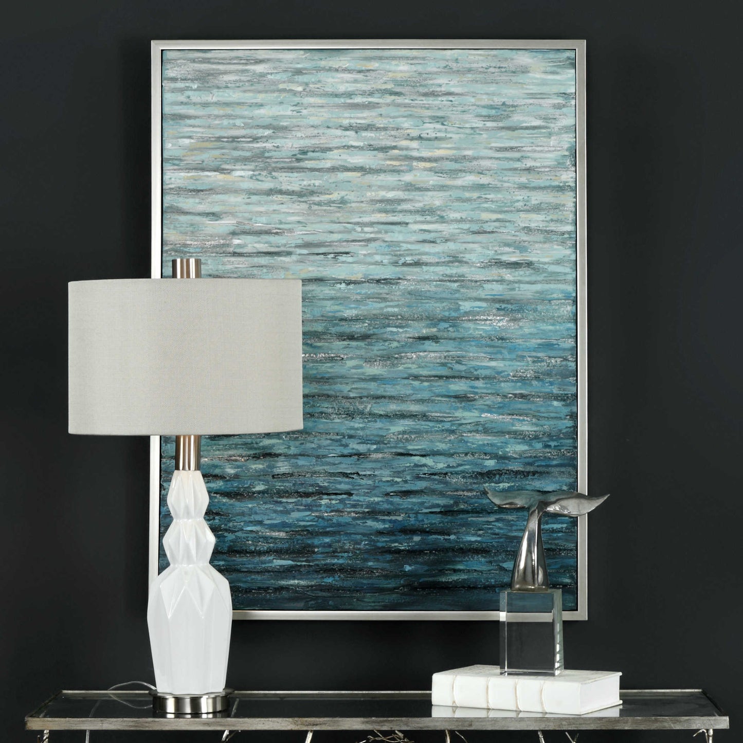 Blue textured print of waves on water that are abstract behind a white lamp and decorative sculpture on a gray background. 