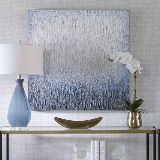 Hand painted piece of white and blue art behind a console with a lamp and white orchid flower.
