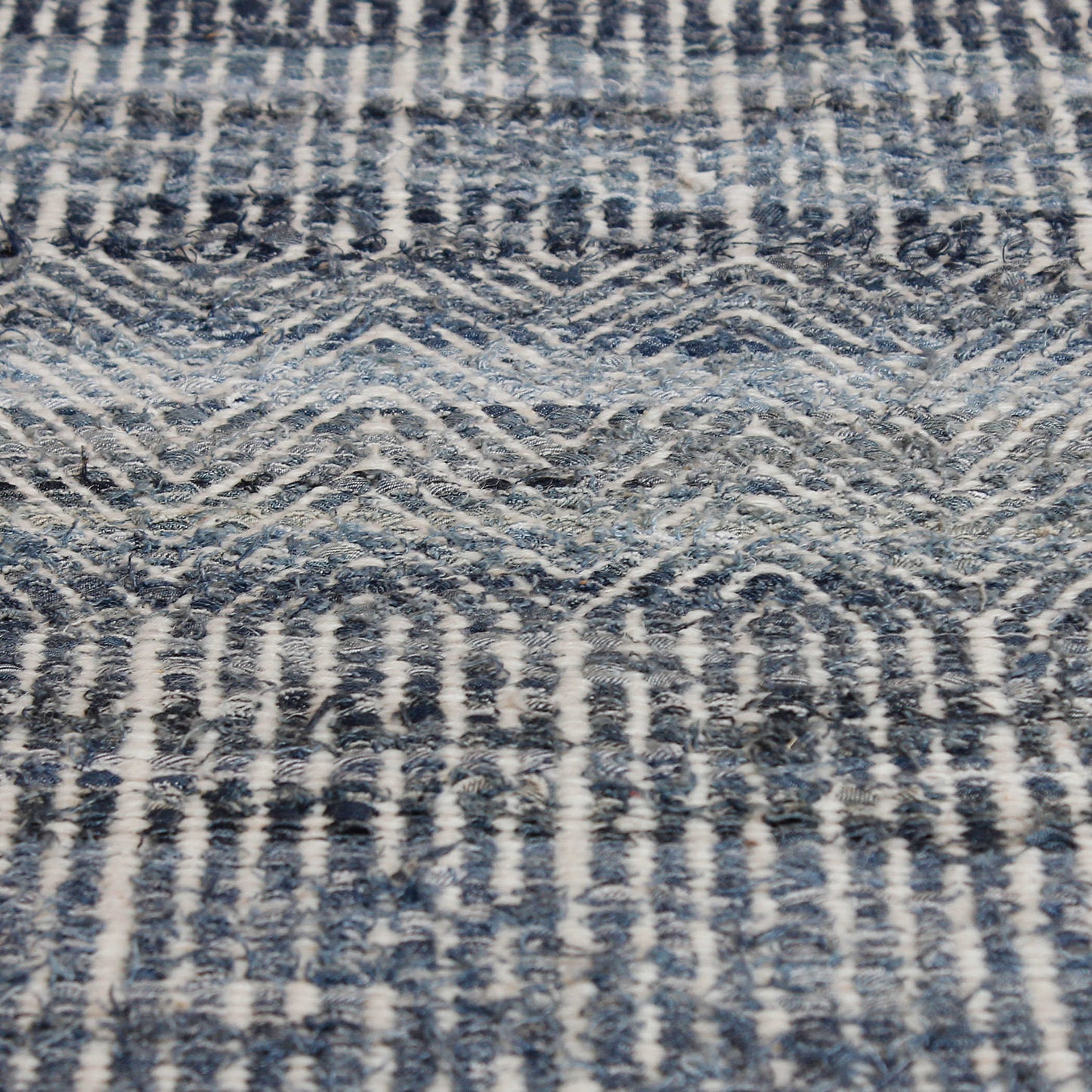 Macro shot of a geometric wool rug with denim fibers and light green and gray fibers. 