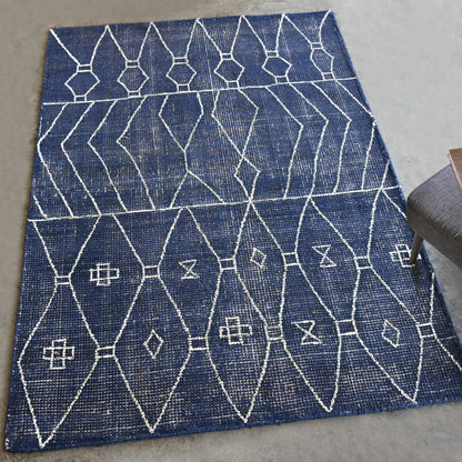 Indigo hand woven rug diagonally on a gray concrete floor next to a gray chair. 
