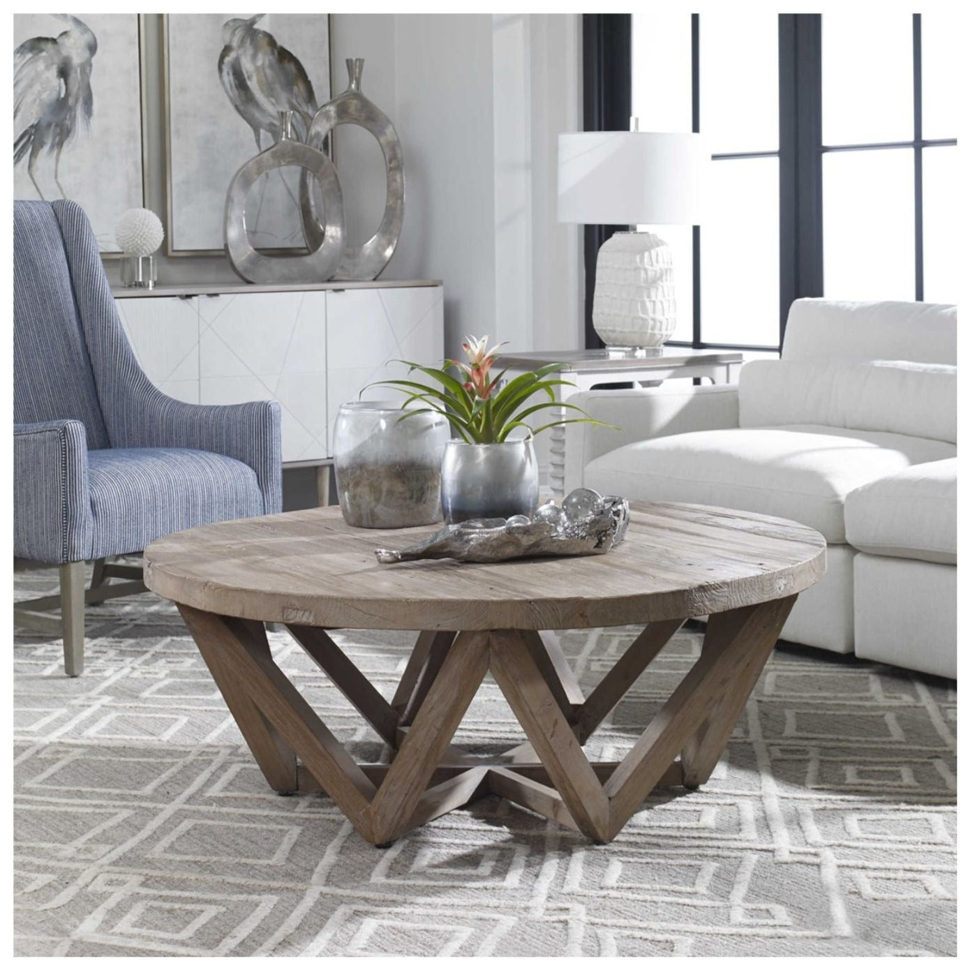 Beautiful reclaimed wood coffee table with tri-angled open legs shown with a sofa, chair and console with art in background.