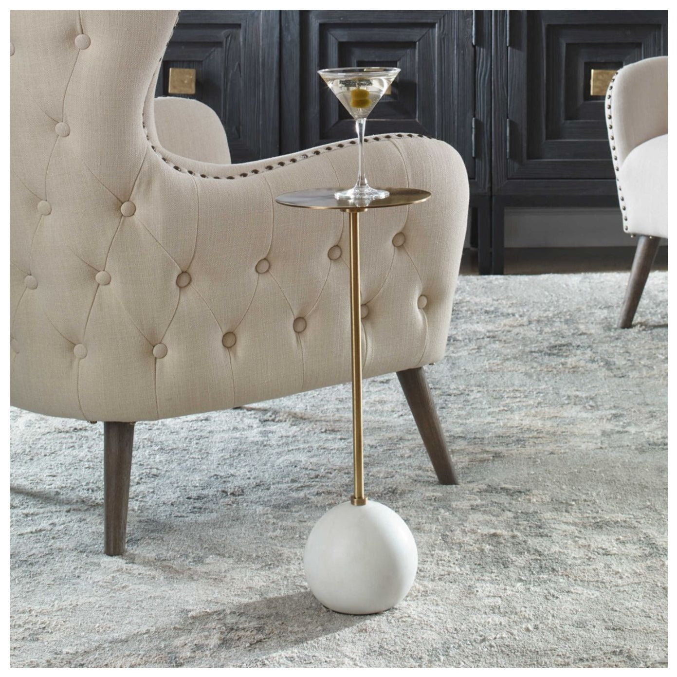 Shows this round marble based drink table with brass stem and round brass top beside a chair. Martini sitting on table.