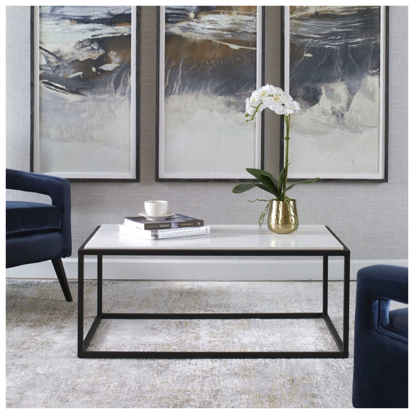 Room setting of this coffee table features a satin black iron frame accentuated by a beautiful inset white marble slab top with two chairs and art in the background.