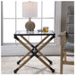 this accent table features a rustic iron frame wrapped in natural fiber rope accents topped with clear tempered glass showing in front of a window next to a table. A lamo decorates table top while a drink and eye glasses rest on the top.