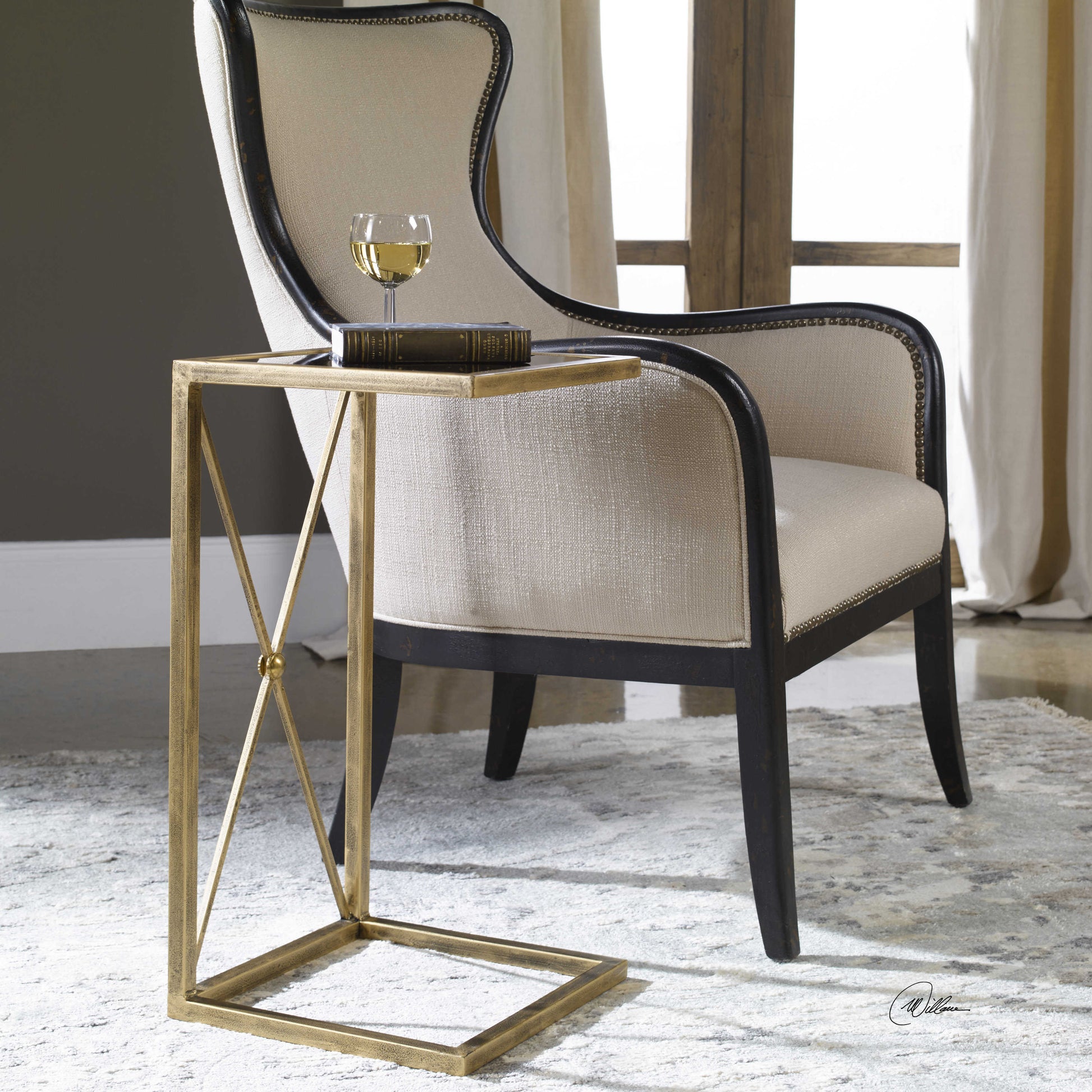 A black and gold end table with a geometric metallic frame and a glass top, placed on a rug next to a chair.