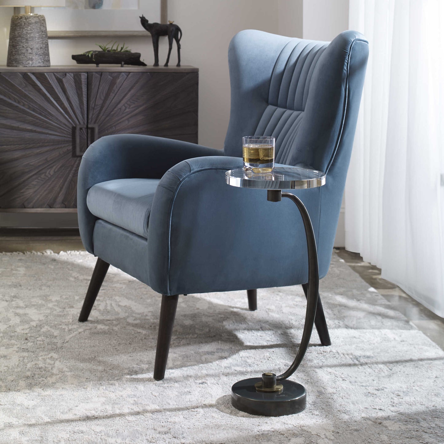 Curved accent table in front of a blue decorative chair in an upscale home interior with strong design.