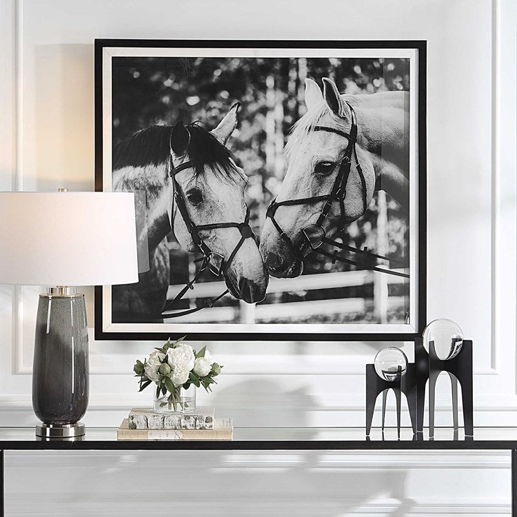 A framed black and white photograph of two horses wearing bridles, displayed in a modern interior setting.