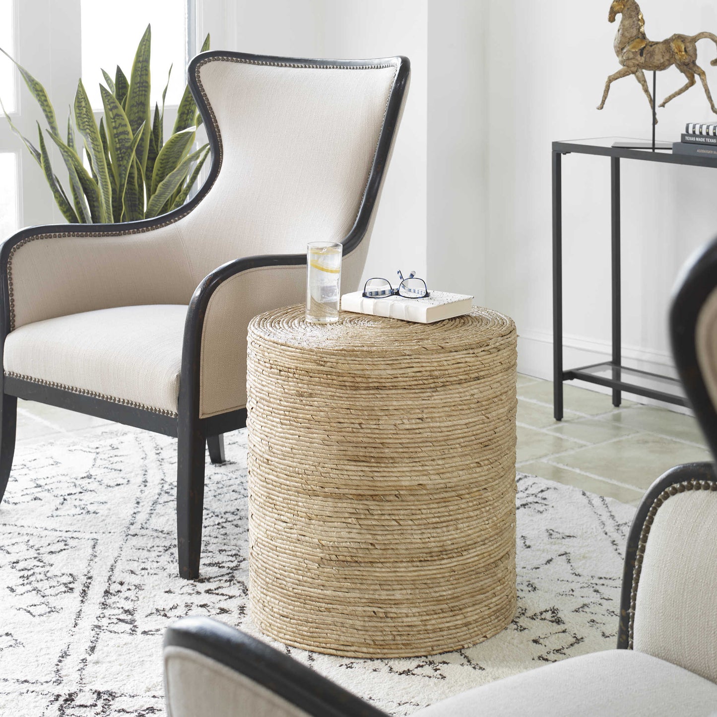 White rug with rattan round end table in a living room with decorative armchairs and a black console with horse sculpture.