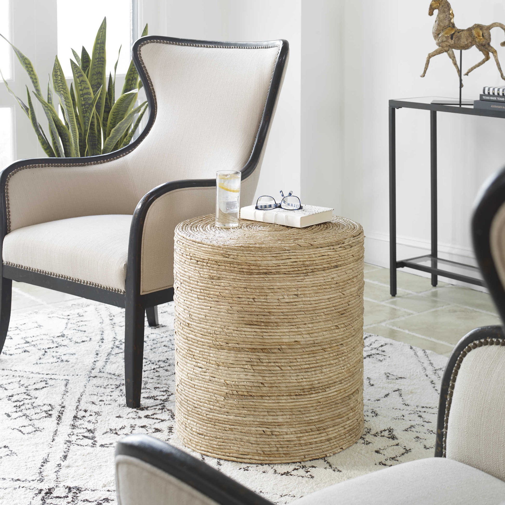 White rug with rattan round end table in a living room with decorative armchairs and a black console with horse sculpture.