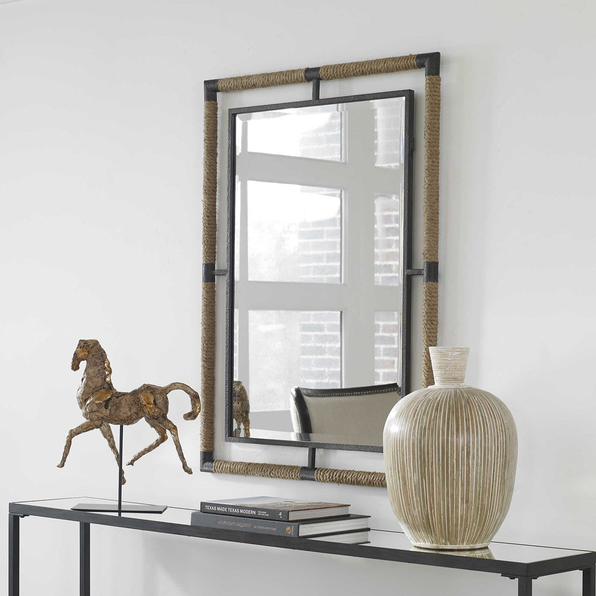 Decorative mirror with a horse sculpture and vase on a console table against a white wall.