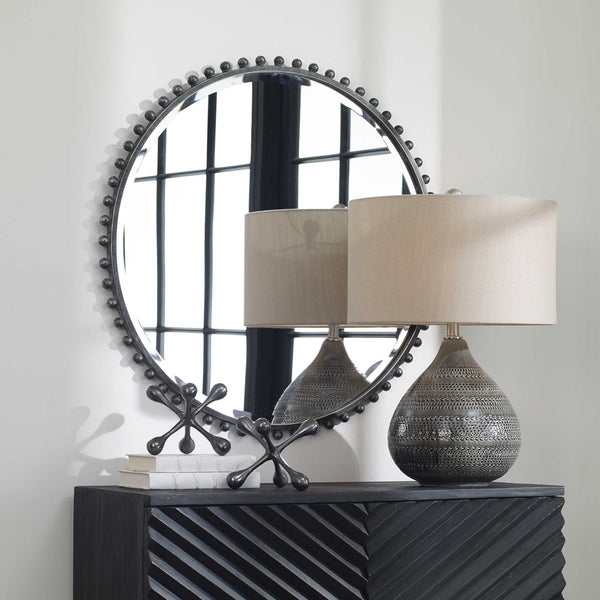 Black iron mirror that is round with decorative spheres / balls around the exterior in a living room above a black console.